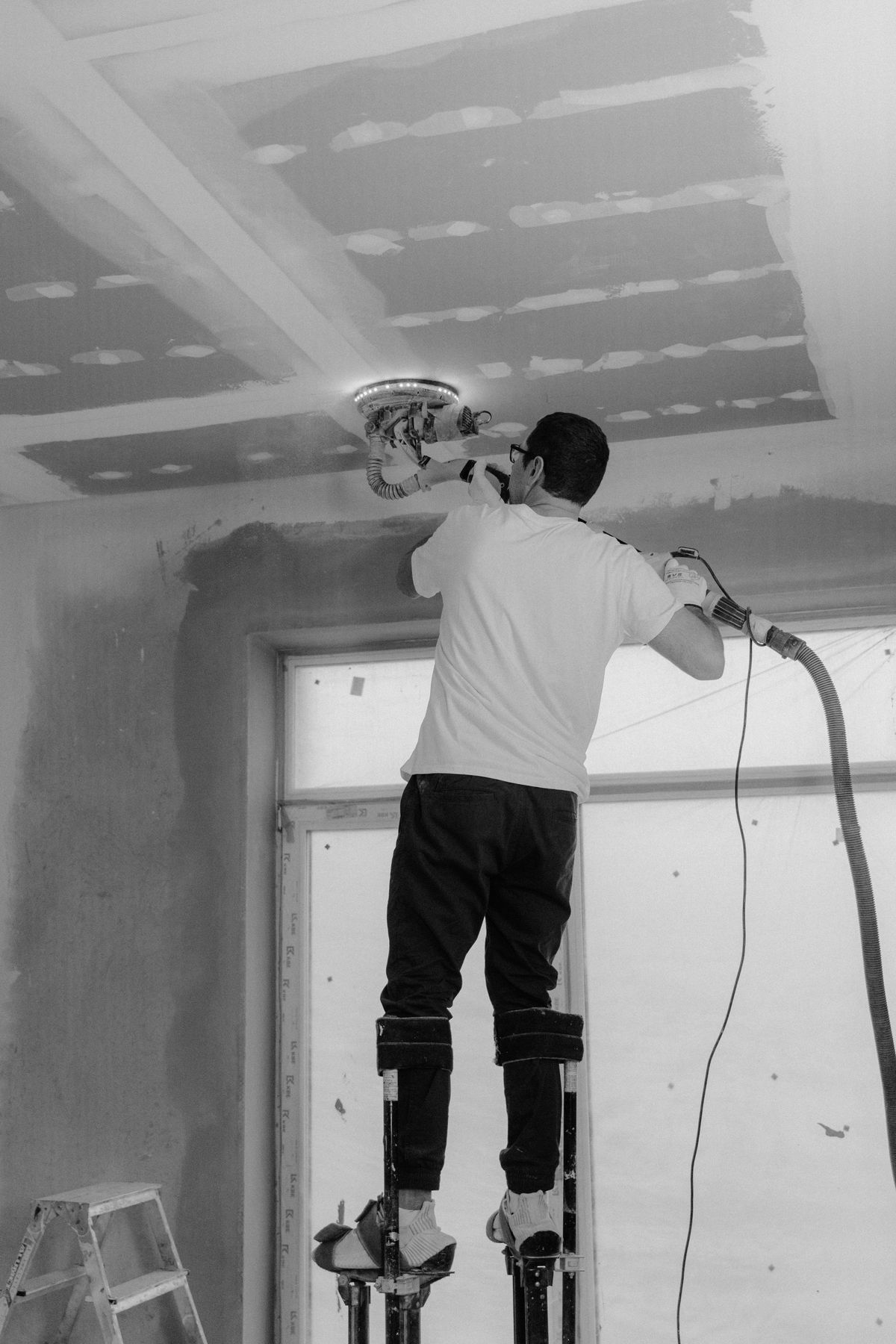 Ceiling professional on stilts smoothing a skim-coated drywall ceiling — the refinishing stage after popcorn texture comes off